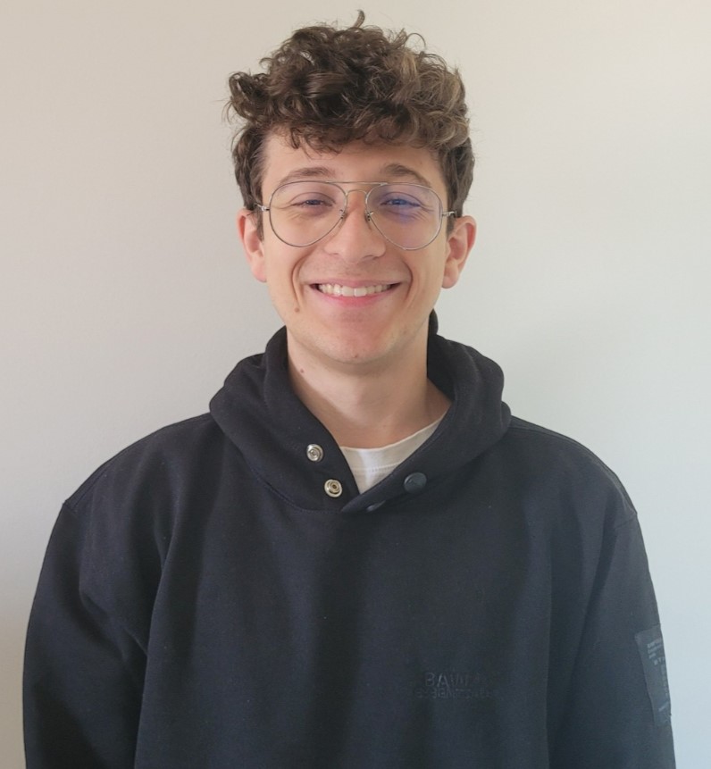 Juan Andrade smiling in a red plaid shirt and tortoise shell glasses